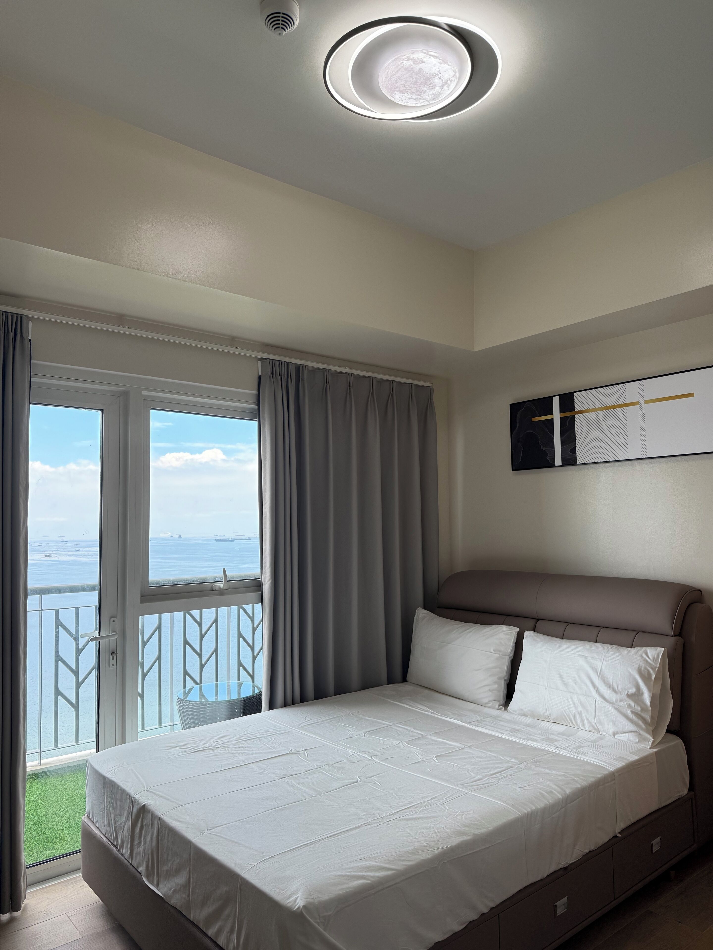 A bedroom with a bed, a view of the sea, and a ceiling light.