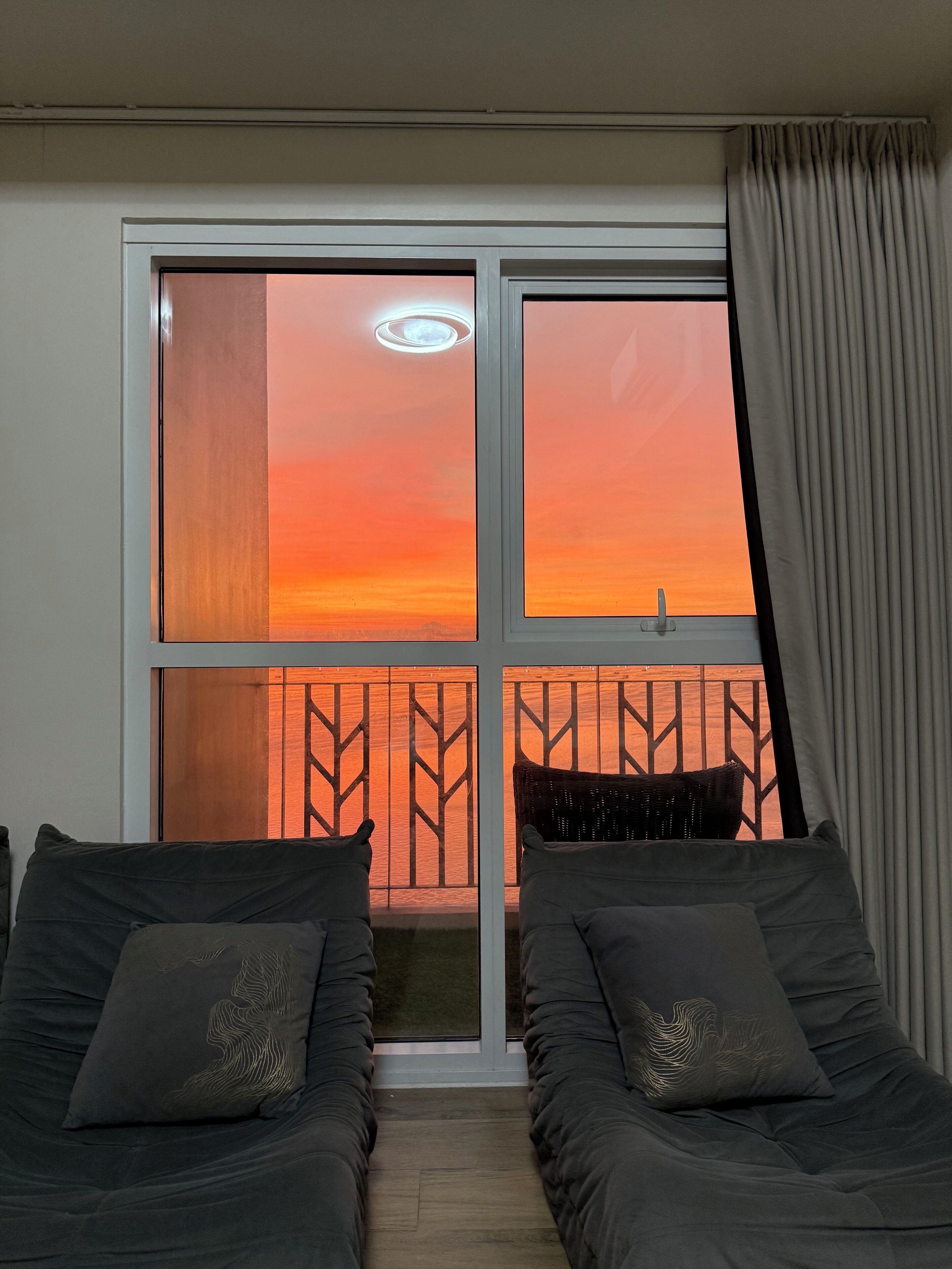 A room with two beds, a window with a view of a sunset, and a curtain.