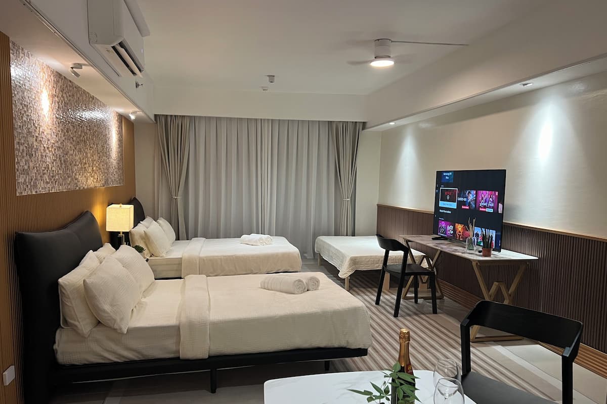 A hotel room with two beds, a desk with a TV, a chair, and a small table with a bottle and glasses.