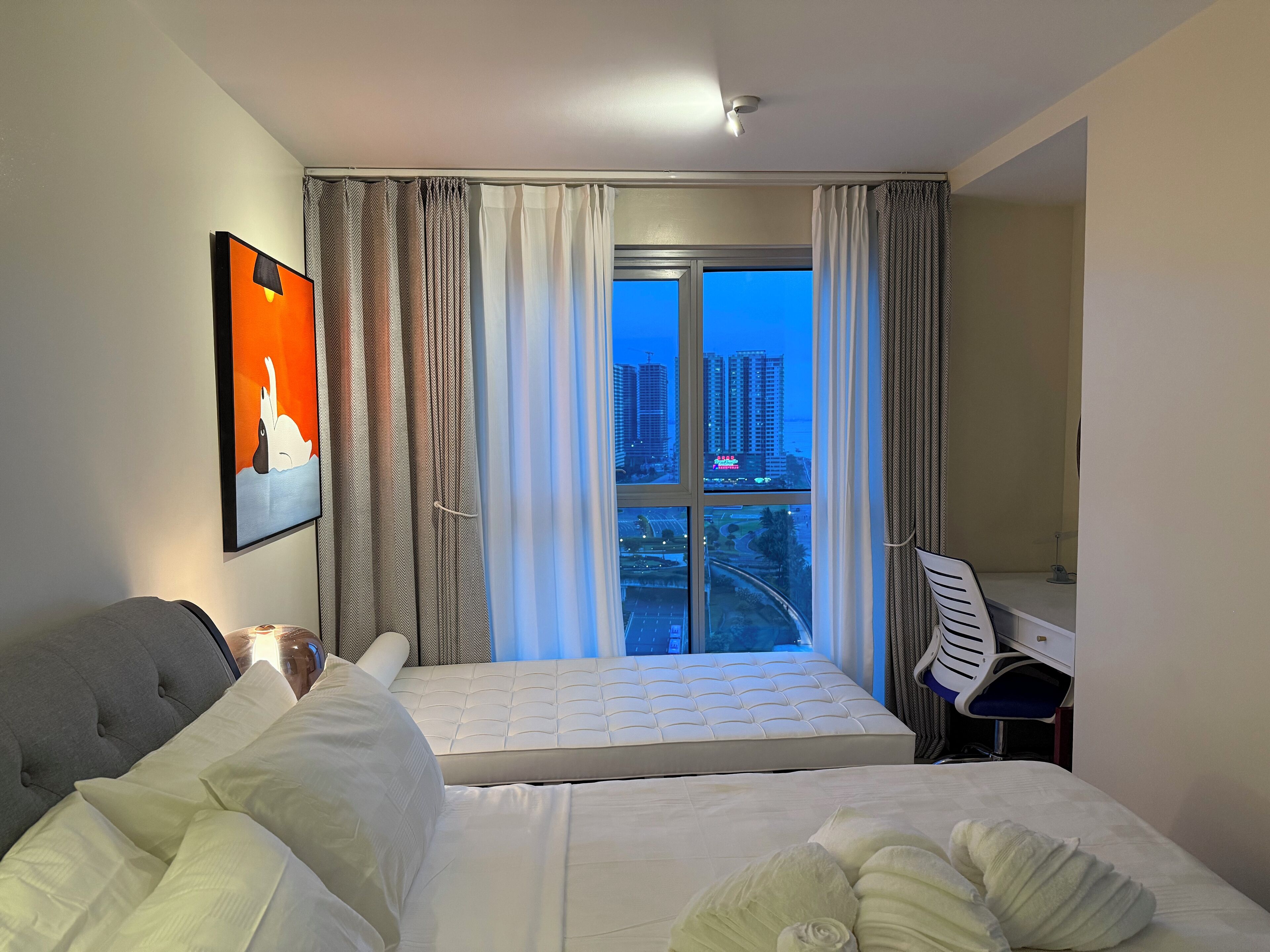 A hotel room with a bed, a desk, and a large window with curtains.