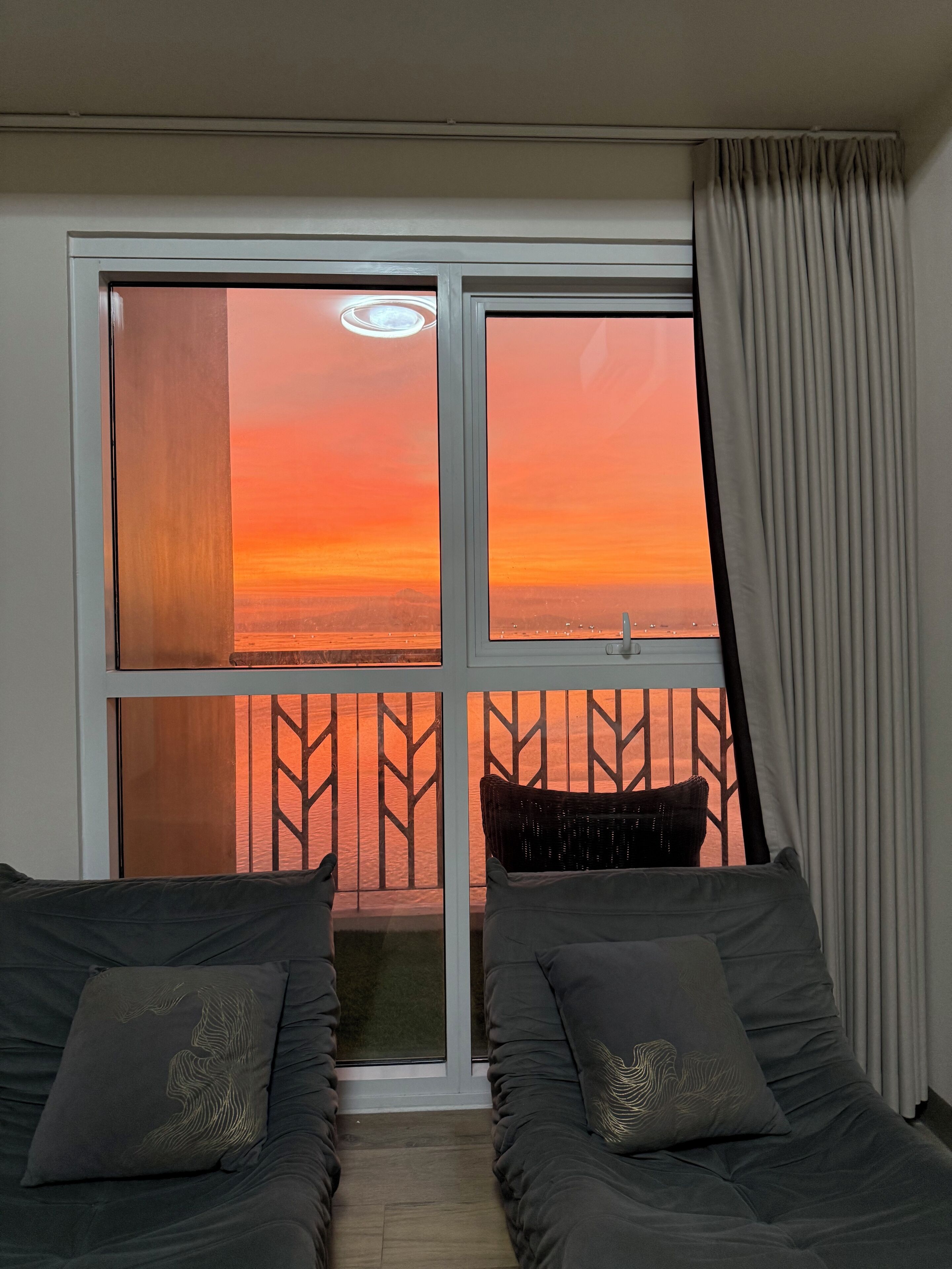 A room with two beds, a view of a sunset, and a sliding glass door.