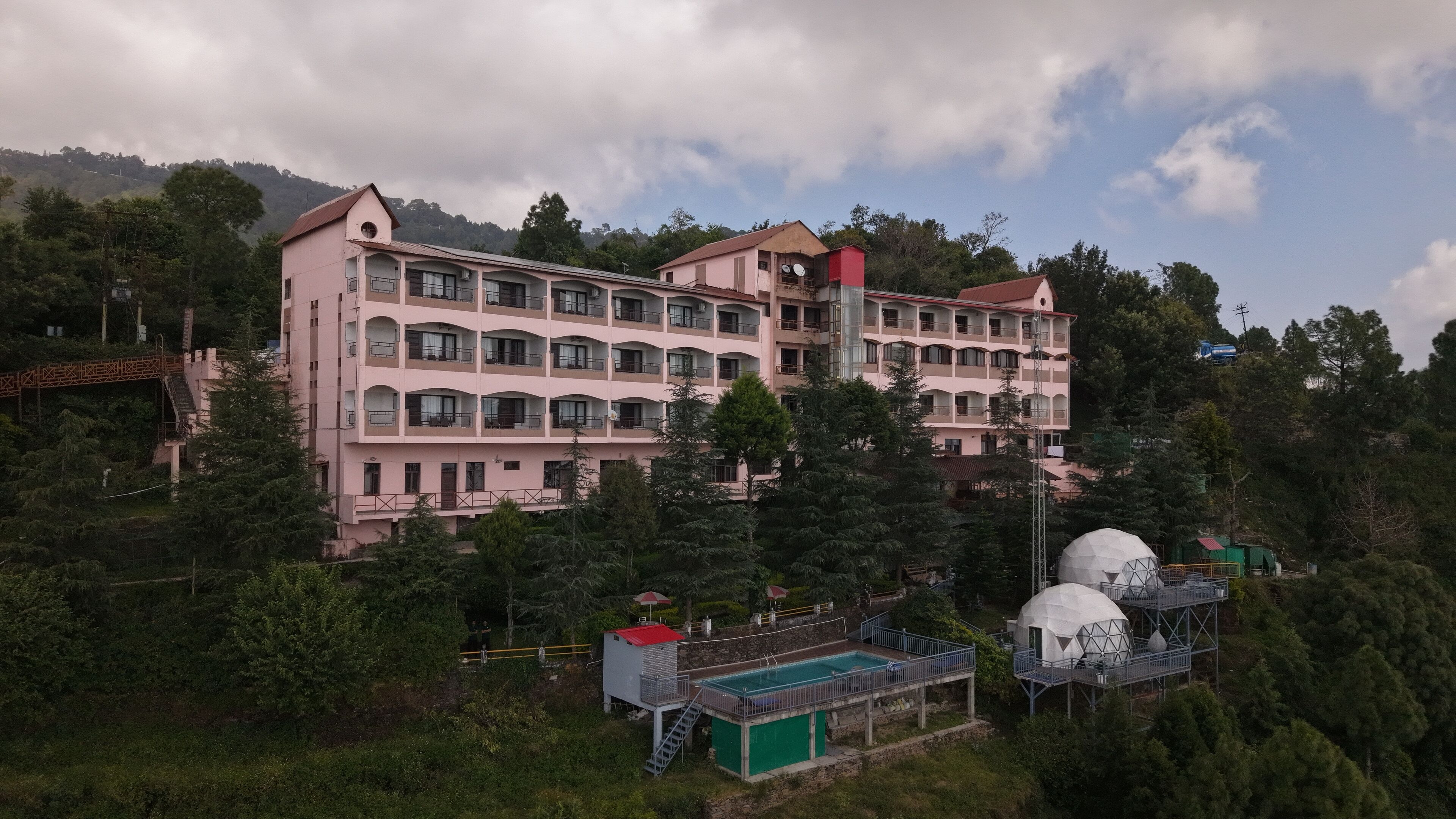 A multi-story hotel with balconies, a swimming pool, and a red-roofed structure.