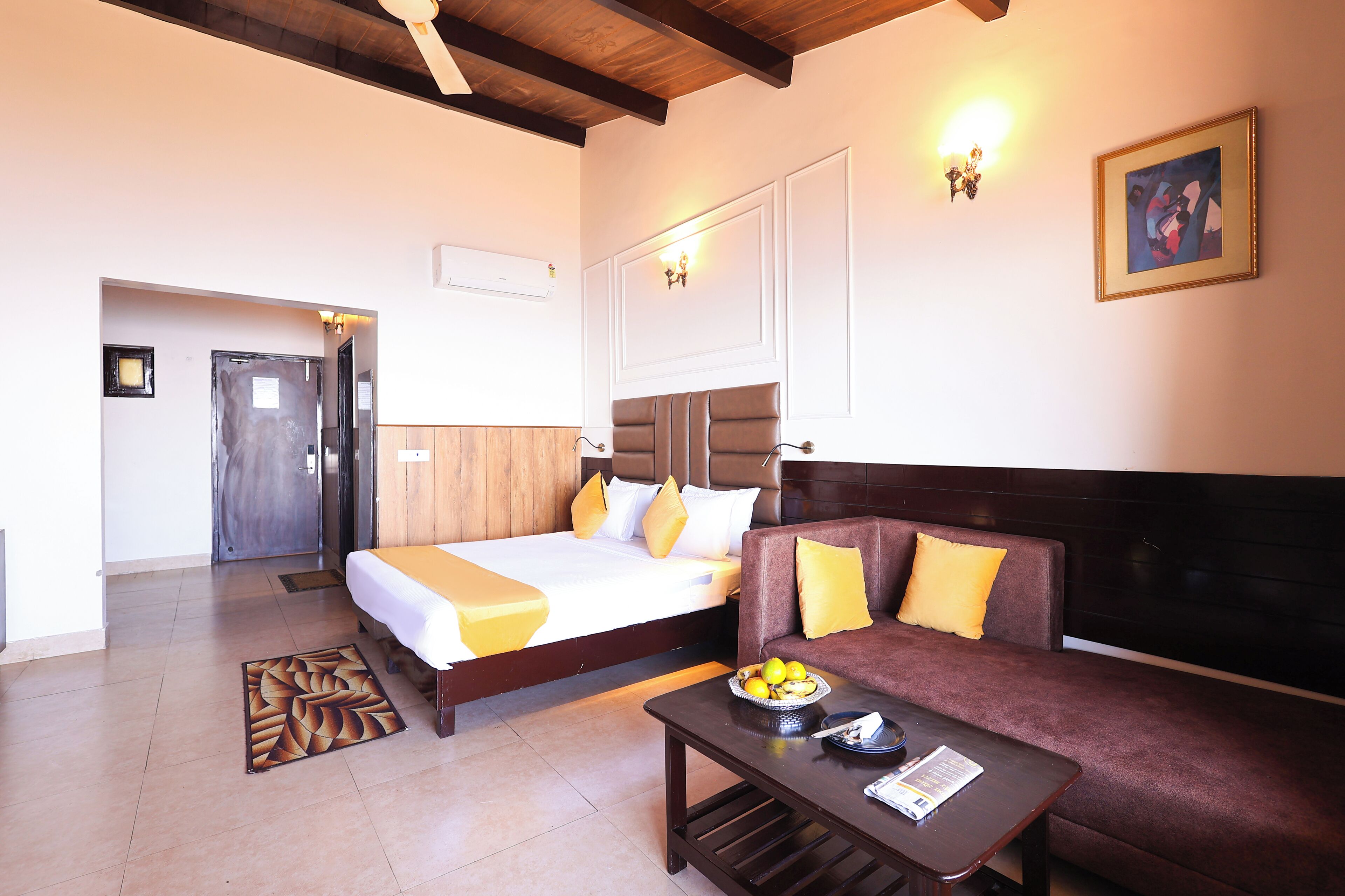 A hotel room with two beds, a sofa, a coffee table with fruits, and a painting on the wall.
