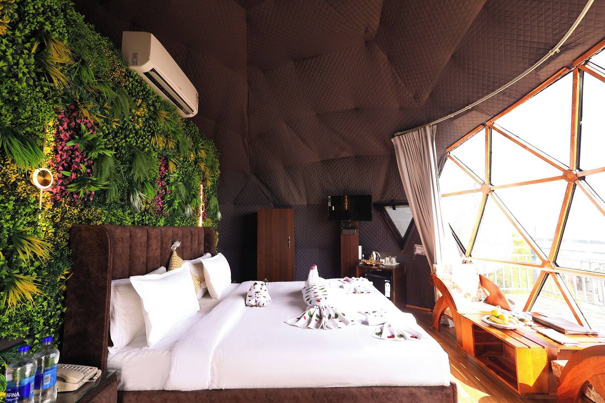 A room with a bed, a TV, a wooden side table, and a large window.