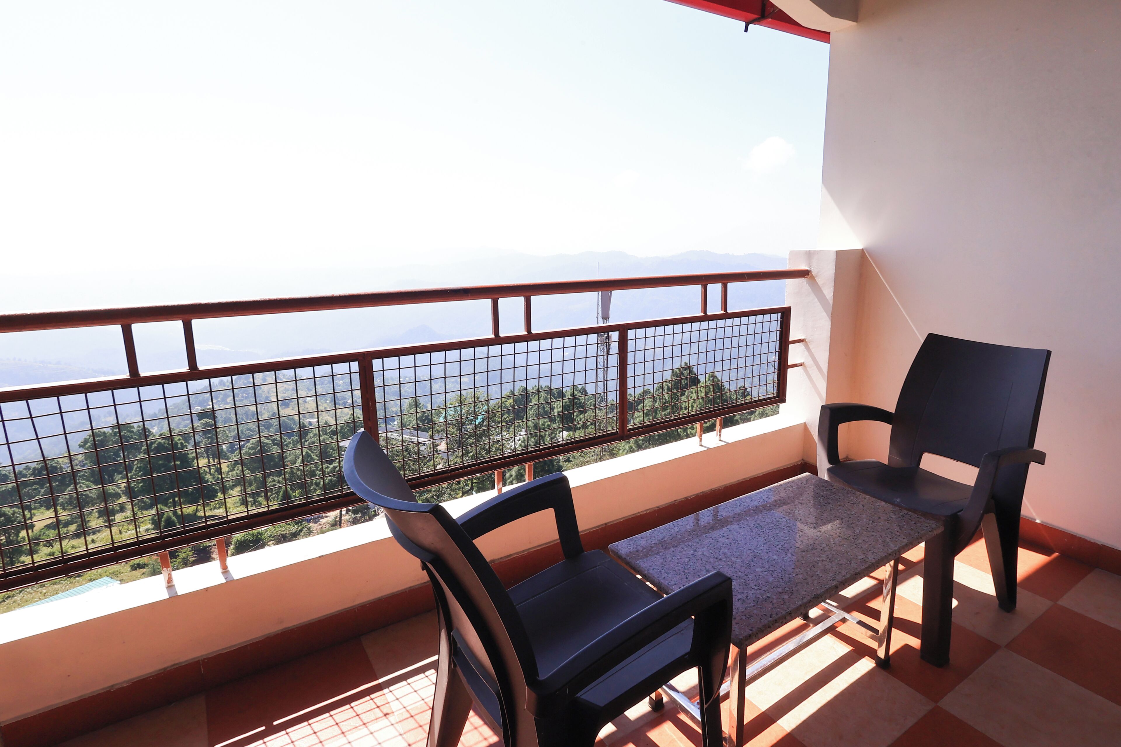 A balcony with a table and two chairs, overlooking a scenic view of mountains and greenery.