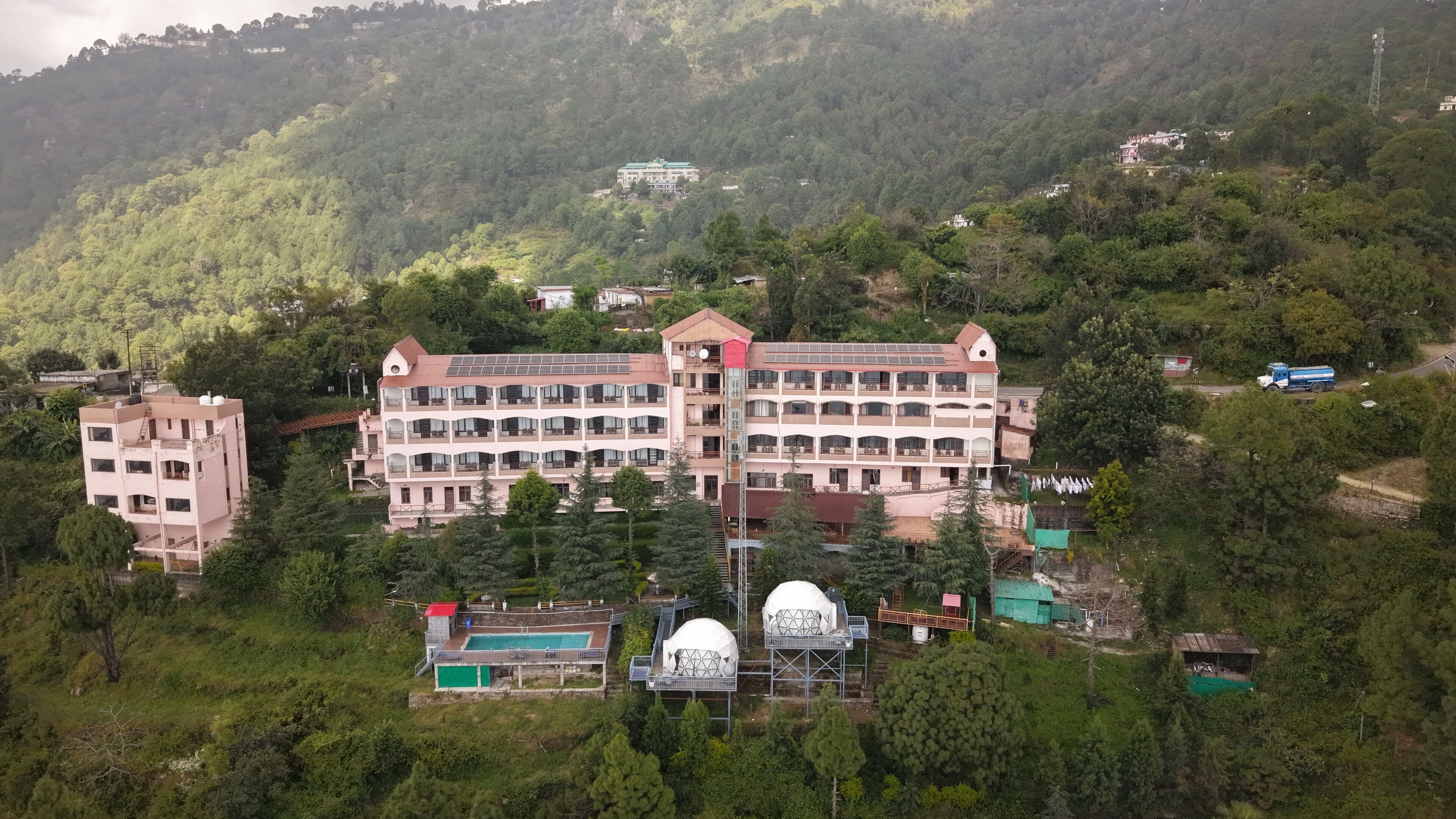 A multi-story hotel with a pool, dome-shaped structures, and a mountainous backdrop.
