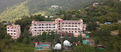 A multi-story hotel with a pool, dome-shaped structures, and a mountainous backdrop.