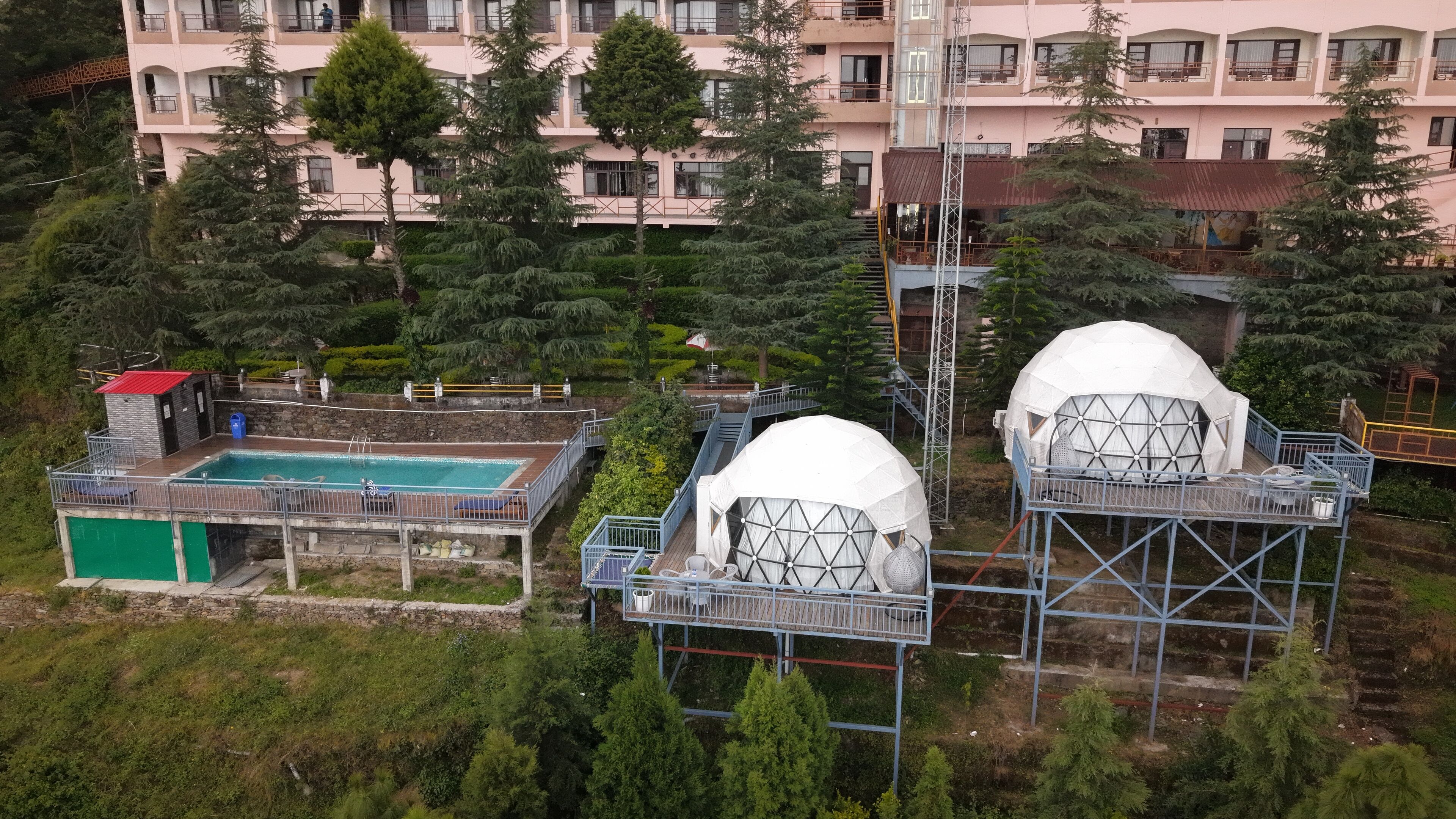 Une piscine avec un petit bâtiment, deux structures en forme de dôme et, au fond, un immeuble à plusieurs étages.