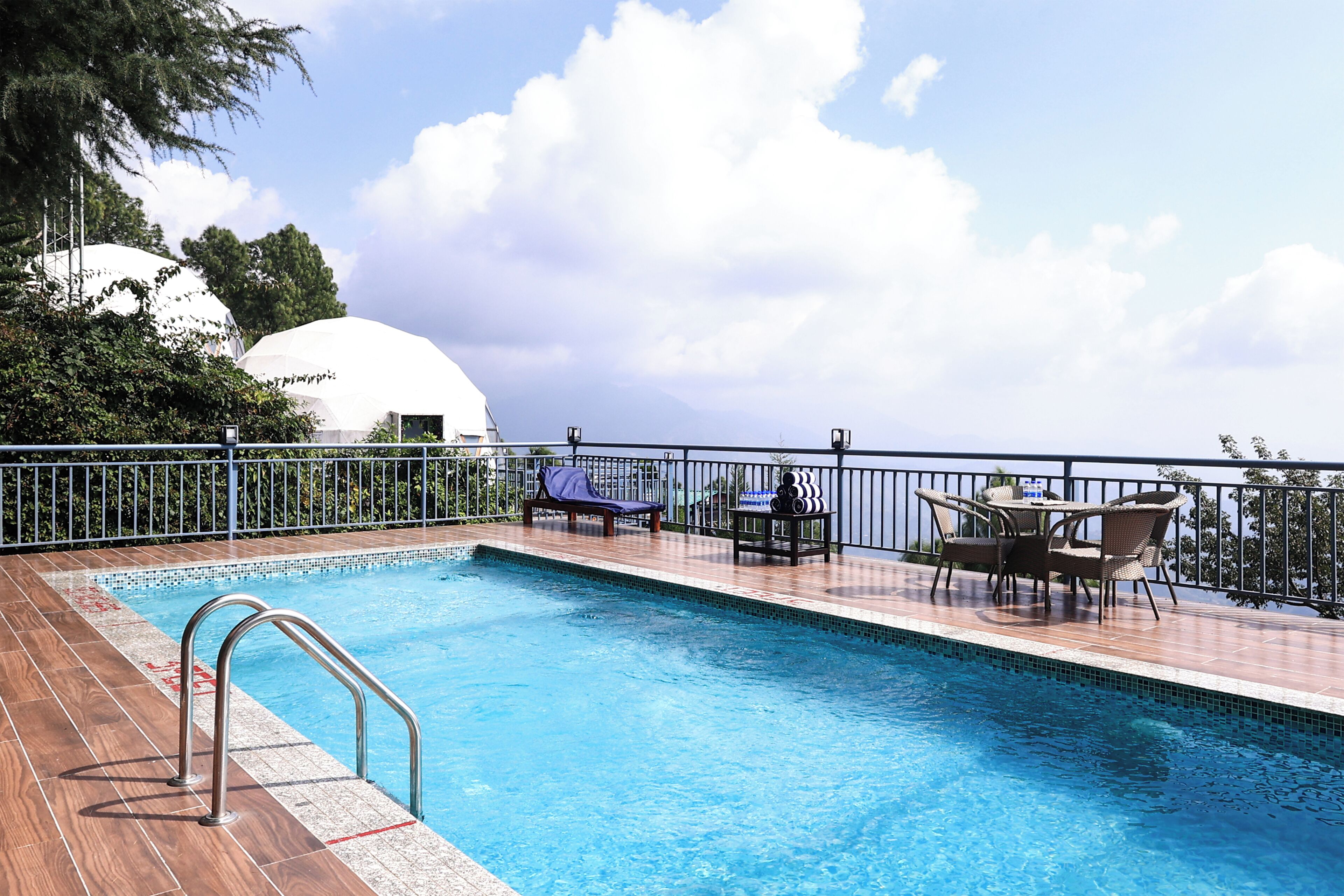 A swimming pool with a wooden deck, lounge chairs, and a table with chairs.