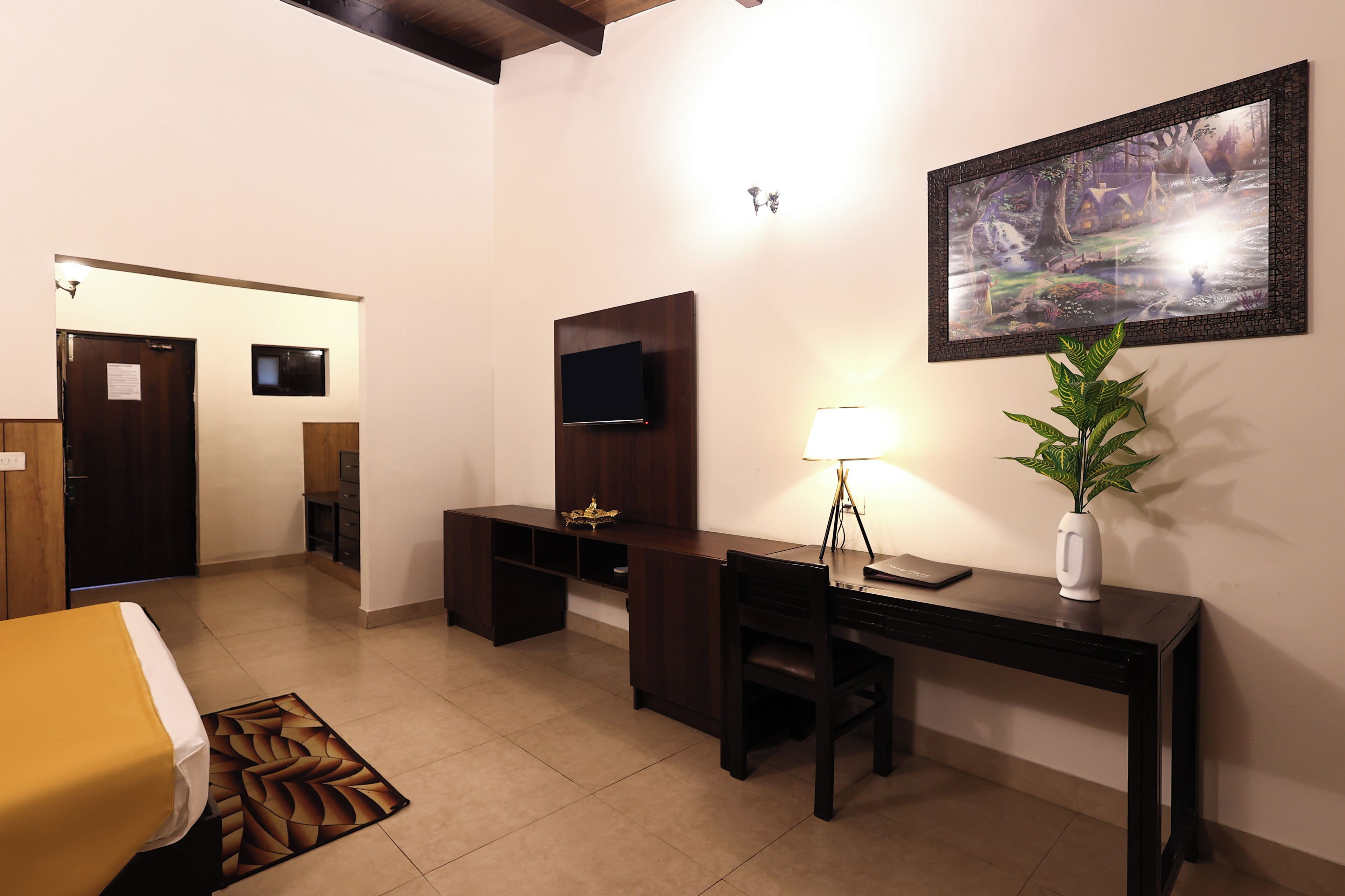 Una habitación de hotel con cama, escritorio, silla, televisor y un cuadro en la pared.