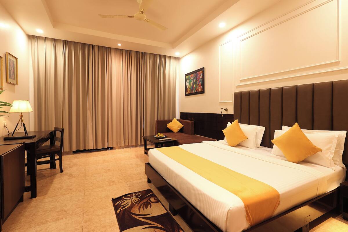 A hotel room with a large bed, a desk, a chair, and a dining table.
