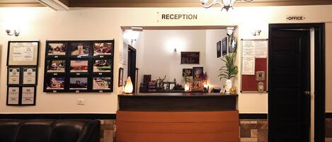 A reception area with a reception desk, framed pictures on the wall, a black door labeled "OFFICE", and a black leather couch.