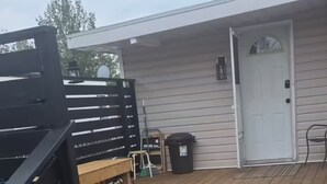 Een houten terras met treden naar een witte deur, een zwart hek en een bank.