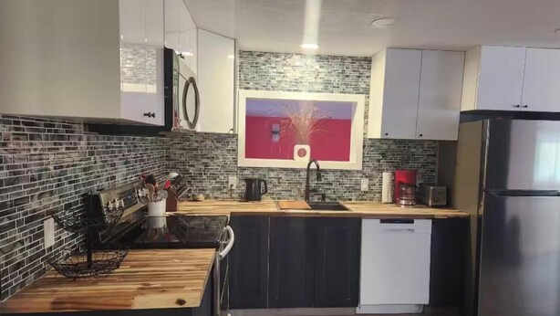 Een moderne keuken met een zwart aanrecht, witte kastjes en een roestvrijstalen koelkast.