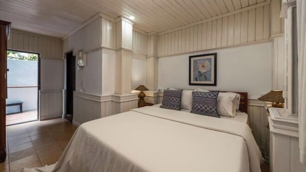 Un dormitorio con una cama, dos lámparas de noche, un cuadro enmarcado en la pared y una puerta que da a un espacio exterior.
