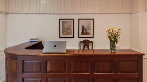Un mostrador de recepción de madera con un portátil, obras de arte enmarcadas en la pared y un jarrón con flores amarillas.