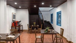 Un área de comedor con mesas y sillas de madera, una escalera y celosías azules decorativas.