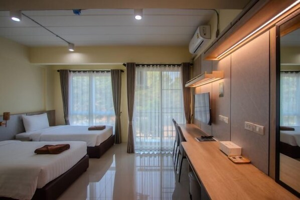 Habitación de hotel con dos camas, un escritorio con una silla, televisión y ventana con cortinas.