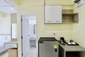 Habitación de hotel compacta con kitchenette, una cama, baño blanco y un pequeño rincón de descanso.