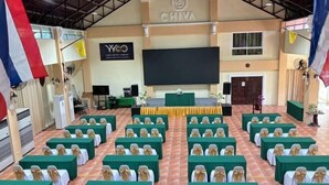 A conference room with rows of chairs, a stage, and a large screen. - Wellness World Chiva Khao Yai (Pak Chong)
