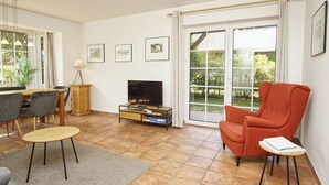 Ein Wohnzimmer mit Fernseher, Esstisch, Stühlen und einem roten Sessel.