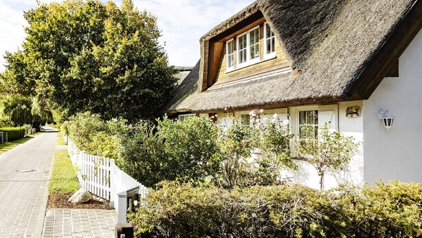 Ein traditionelles Haus mit einem Strohdach, weißen Wänden und einem Holzrahmenfenster.