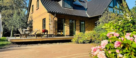 A house with solar panels on the roof, a brick exterior, and a wooden deck with outdoor furniture.