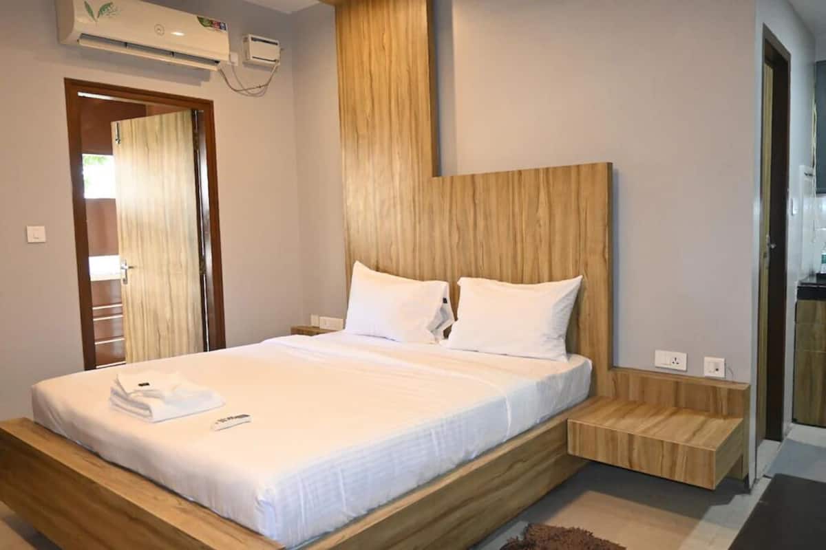 A modern bedroom with a wooden headboard, a bed with white linens, and a small wooden bench beside the bed.