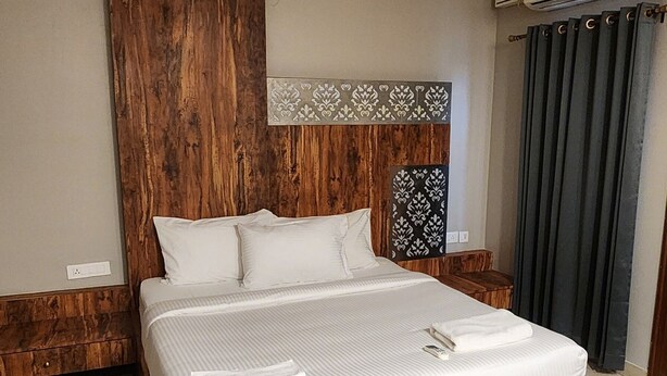 A modern bedroom with a wooden bed frame, a headboard with a patterned design, and a large window with curtains. - ZIPP Lite Frazer Town  (Bengaluru)