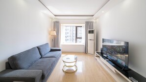A modern living room with a grey sofa, a small round table, a flat-screen TV, and a window with curtains. - Tyms 2BR APT Xujiahui Dacheng Residence (Shanghai)