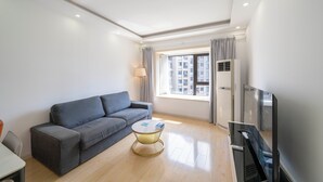 A modern living room with a grey sofa, a small round coffee table, a flat-screen TV, and a window with curtains. - Tyms 2BR APT Xujiahui Dacheng Residence (Shanghai)