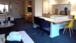 Una habitación de hotel con cama, escritorio, silla, una mesita y kitchenette.