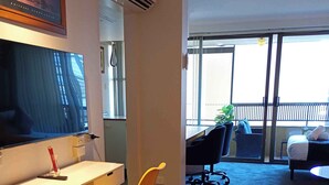 Habitación de hotel con cama, escritorio, silla, televisor y balcón con vistas.