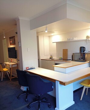 Una cocina compacta con una isla central, un comedor con una silla y una pequeña mesa.