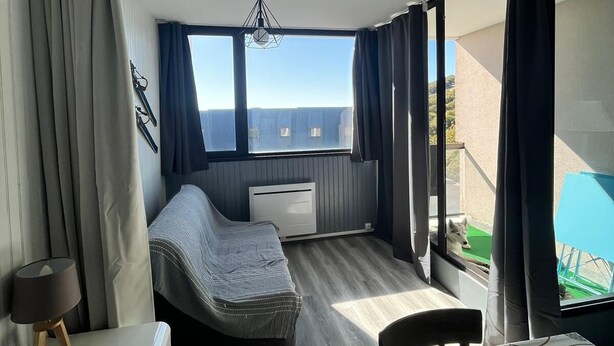 A compact room with a bed, a small table, and a view of the outdoors. - Apartment resort ÔMyrtilles (Besse-et-Saint-Anastaise)