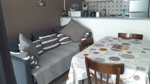A cozy living area with a sofa and a dining table, a kitchen with a refrigerator and a microwave, and a wall with a poster. - Apartment resort ÔMyrtilles (Besse-et-Saint-Anastaise)