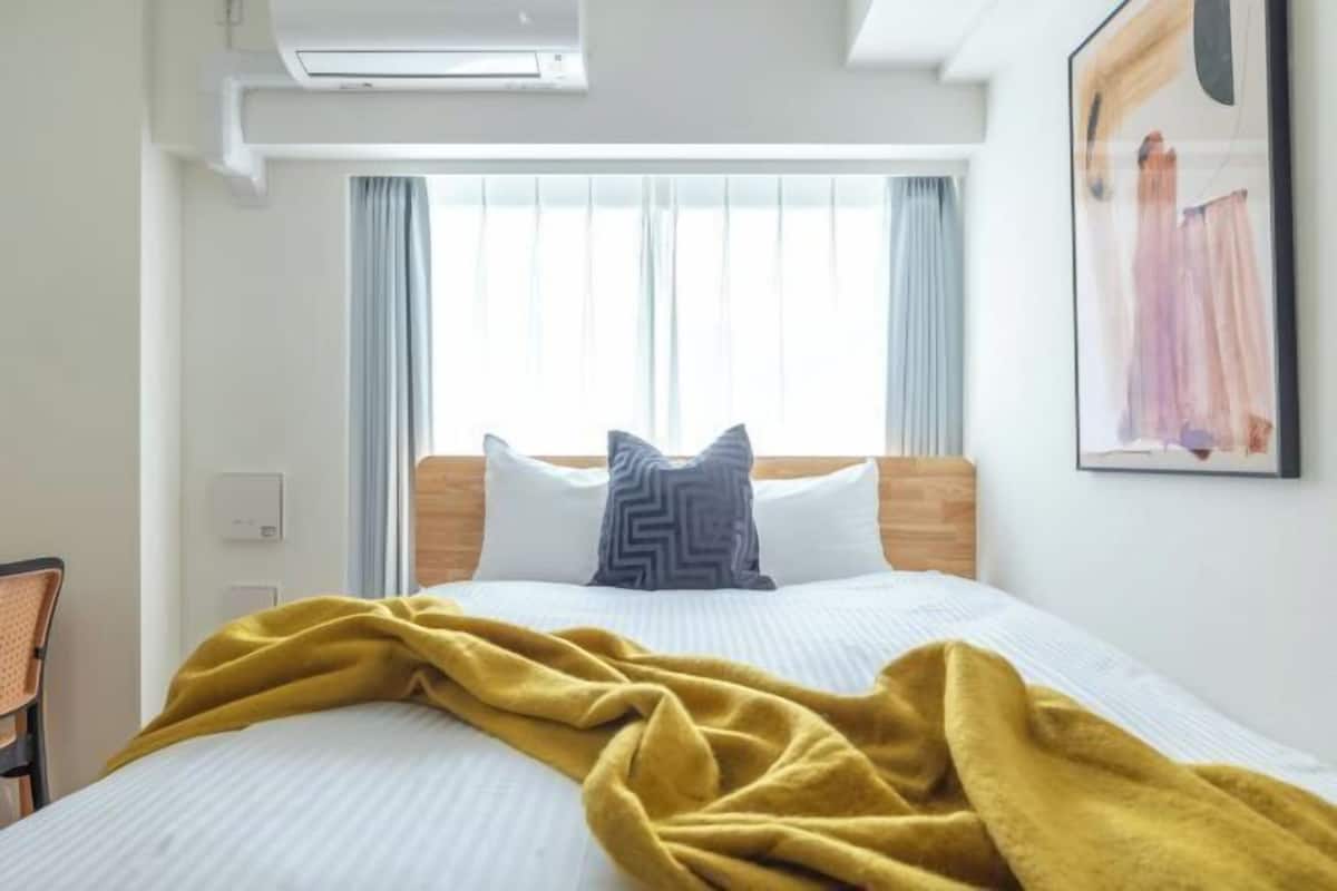 Quarto de hotel com cama, janela com cortinas, ar-condicionado fixado na parede e um quadro emoldurado.
