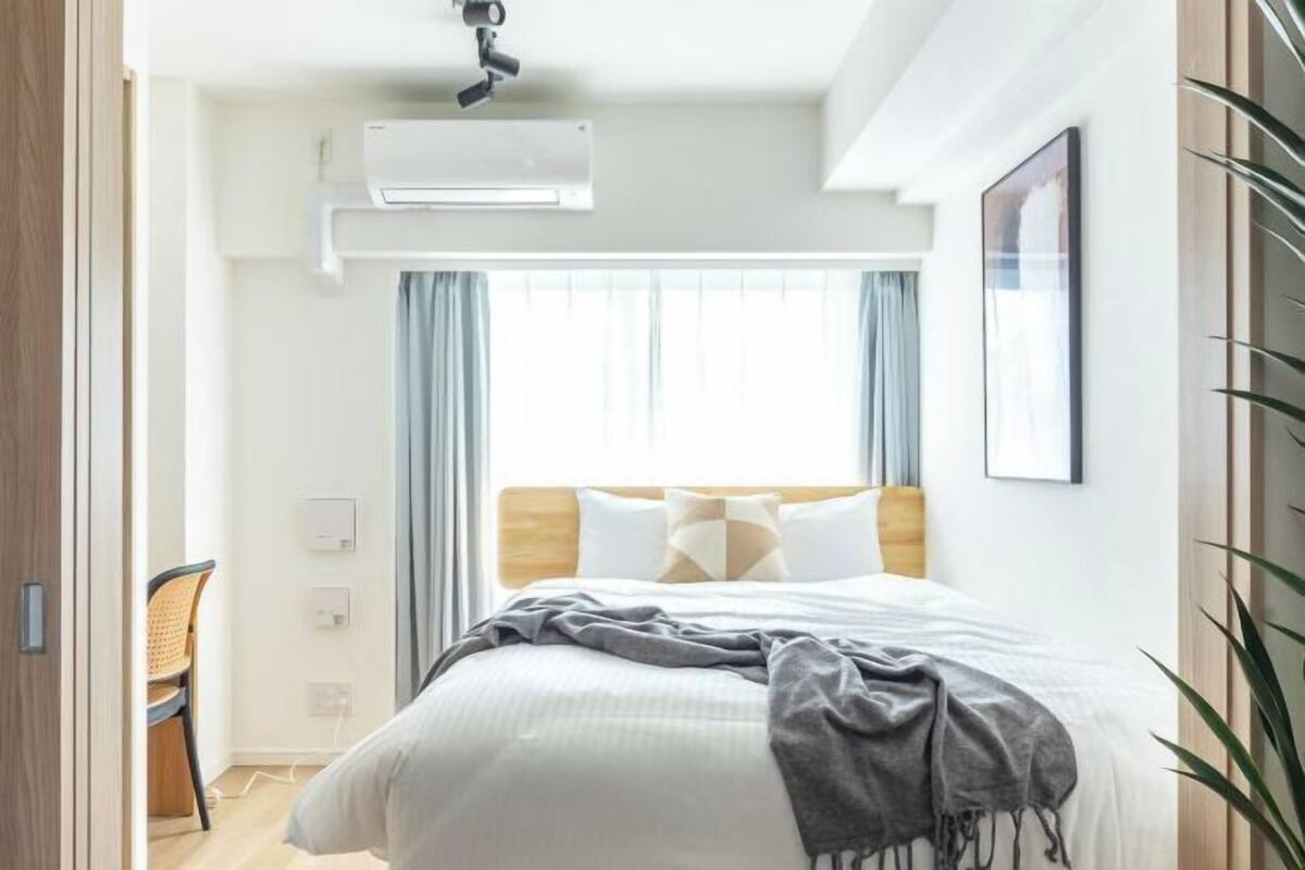 Quarto de hotel moderno com uma cama grande, ventilador de teto, ar condicionado, janela com cortinas e um quadro na parede.