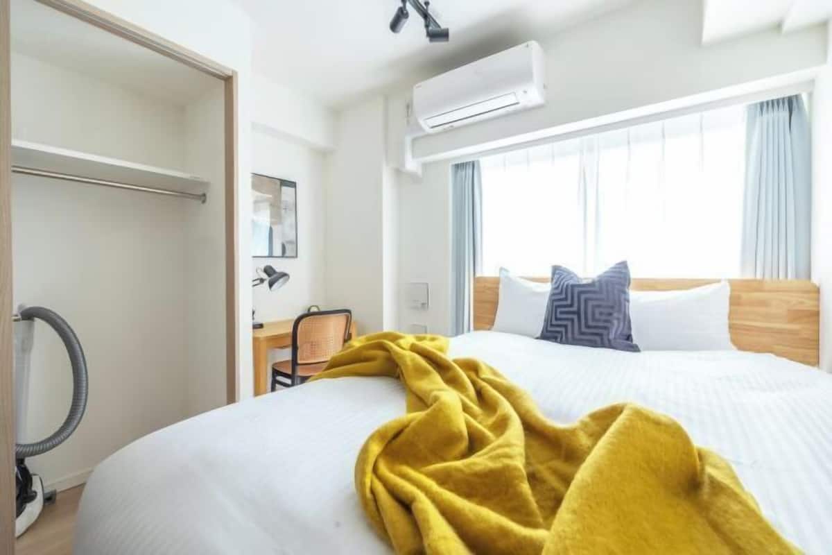 Quarto de hotel com cama, escrivaninha, ar condicionado e janela com cortinas.