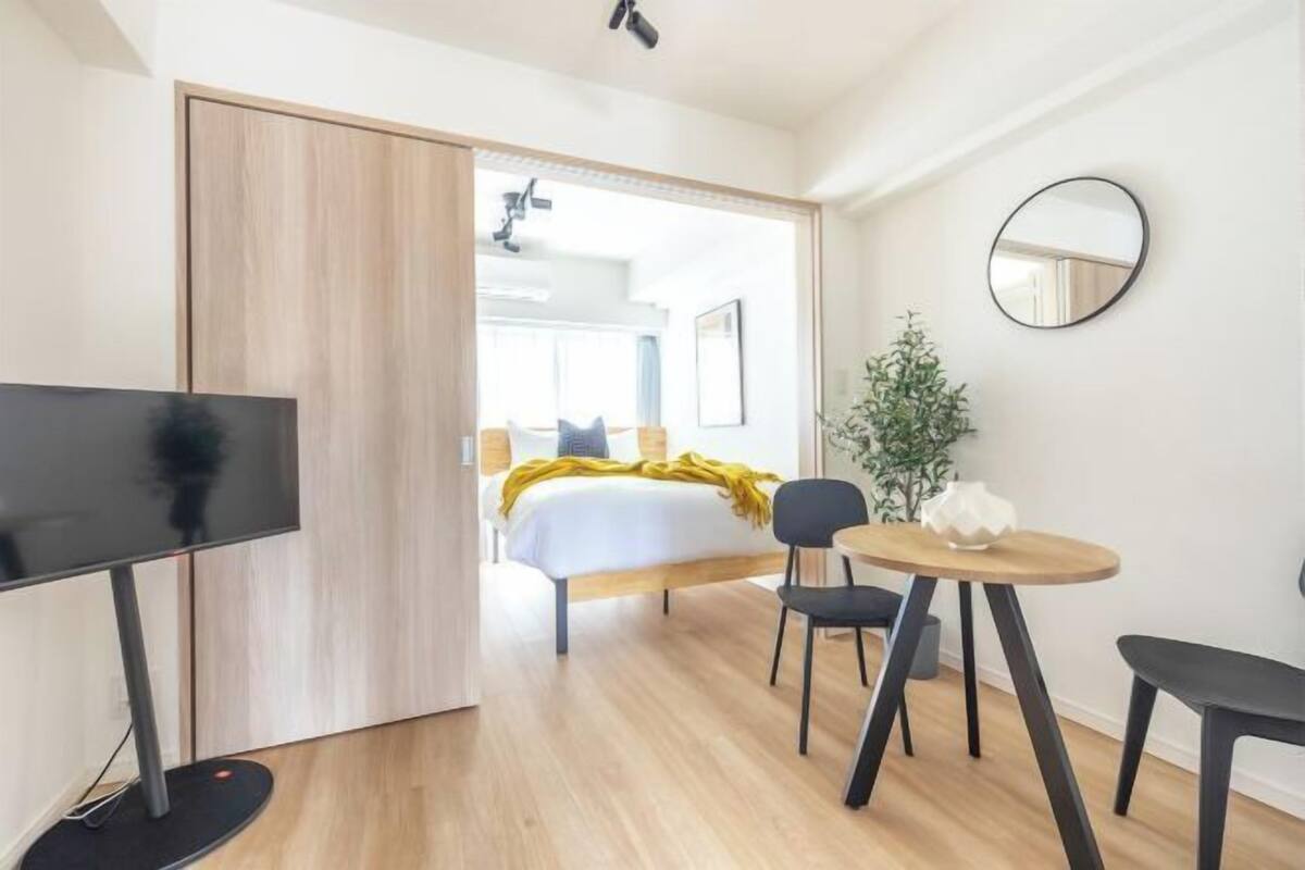 Quarto de hotel moderno com cama, televisão, mesa de jantar e espelho.