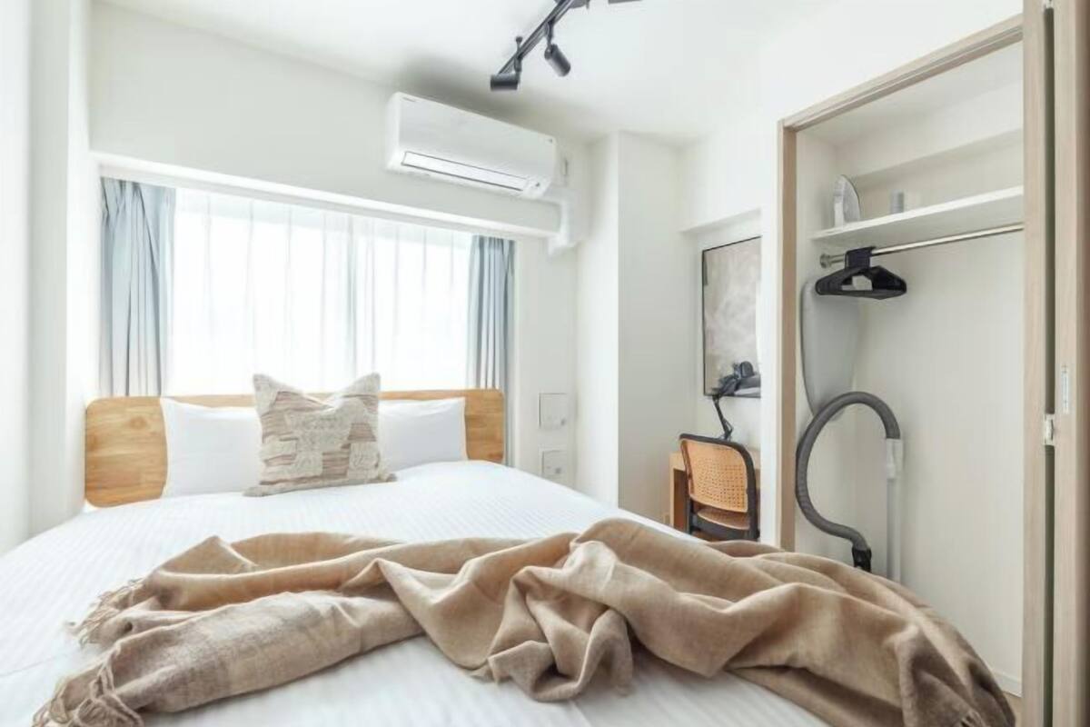 Quarto de hotel com cama, janela com cortinas, ar condicionado, armário com cabides e aspirador de pó.