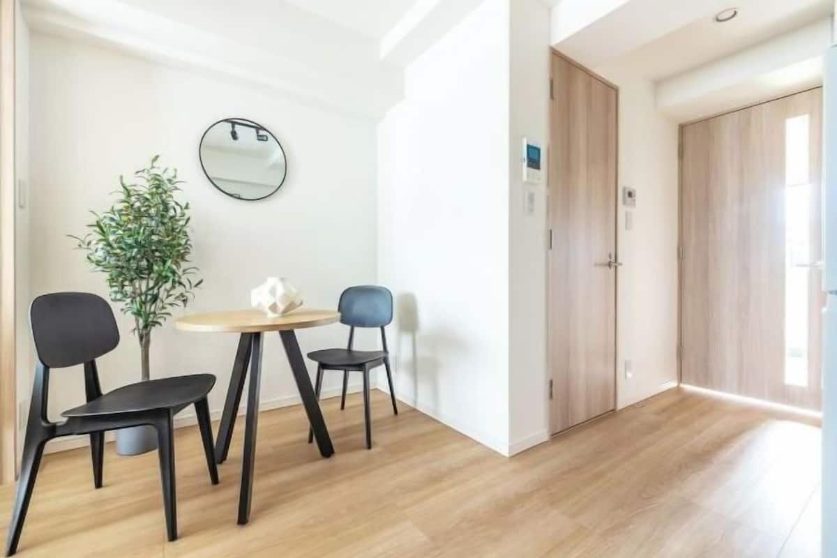 Um quarto moderno com piso de madeira, uma mesa redonda com duas cadeiras, uma planta em vaso e um espelho na parede.