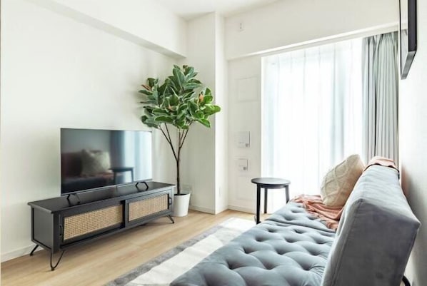 Un soggiorno moderno con una TV a schermo piatto, un divano, una pianta in vaso e un'ampia finestra con tende.