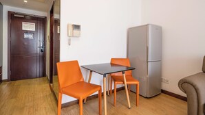A room with a wooden floor, a table with four orange chairs, a silver refrigerator, and a door with a notice. - Tyms Xuhui Elegant 1BR APT  (Shanghai)