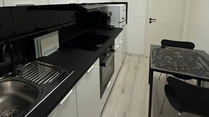 A modern kitchen with white cabinets, a black countertop, and a built-in oven. There is a dining table with chairs and a white door in the background.