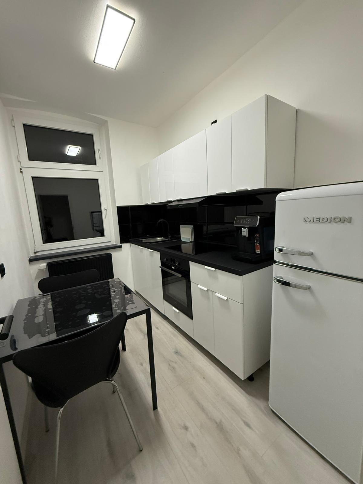 A modern kitchen with white cabinets, a black countertop, a refrigerator, and a dining area with a table and chairs.