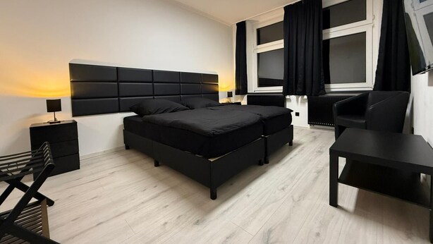 A modern bedroom with a large bed, a desk, and a TV.