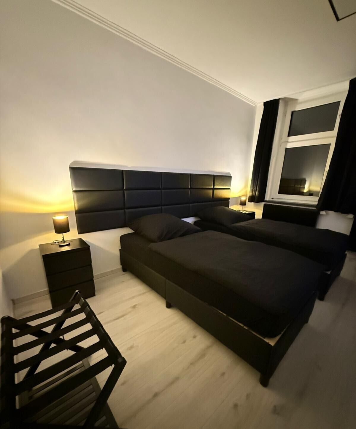 A modern bedroom with a large bed, bedside tables, and a wooden chair.