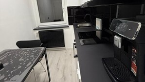 A compact kitchen with a window, a built-in oven, a coffee machine, and a small dining table.