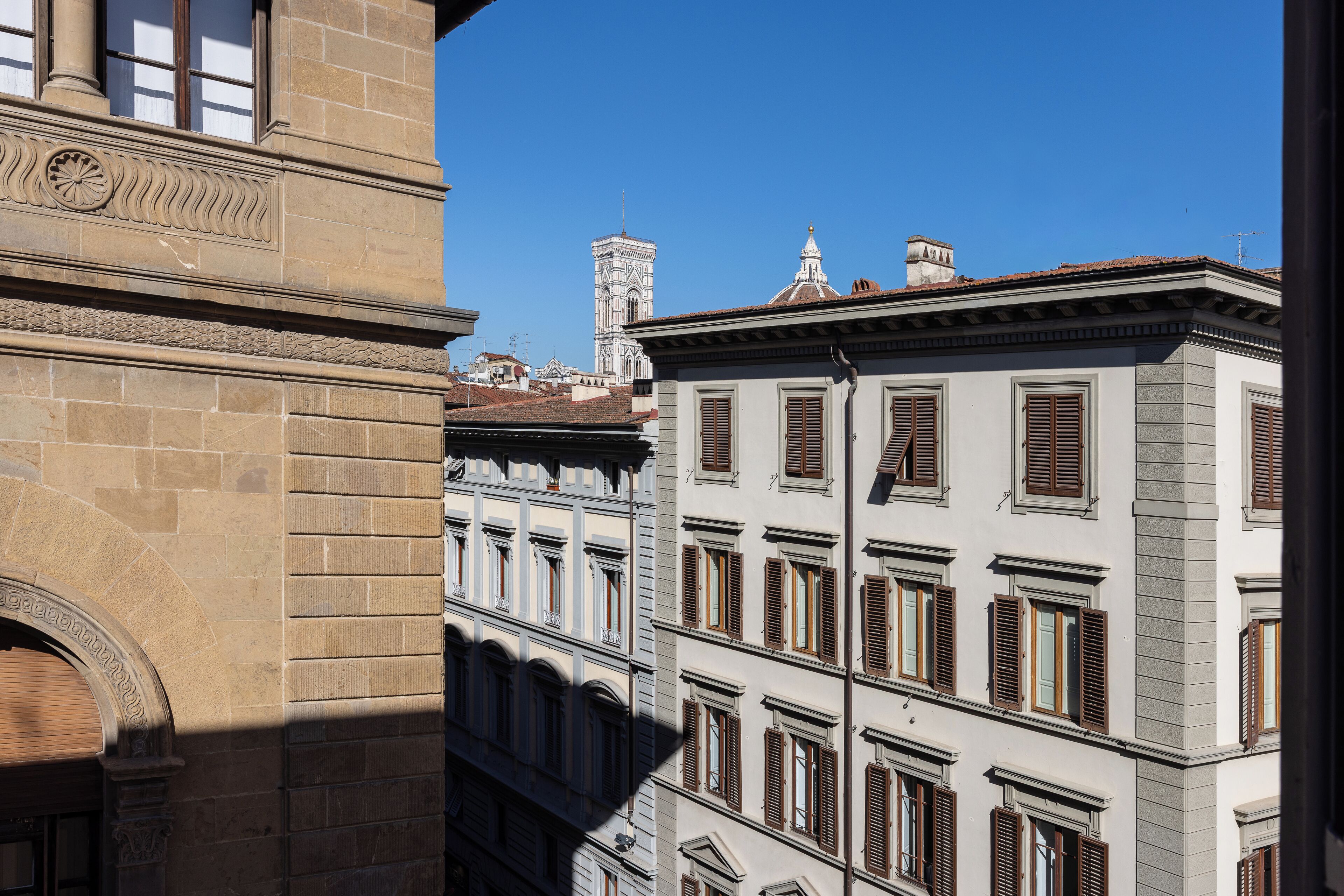 Ein historisches Gebäude mit einem Glockenturm, mehreren Fenstern mit Fensterläden und wolkenlosem, blauem Himmel.